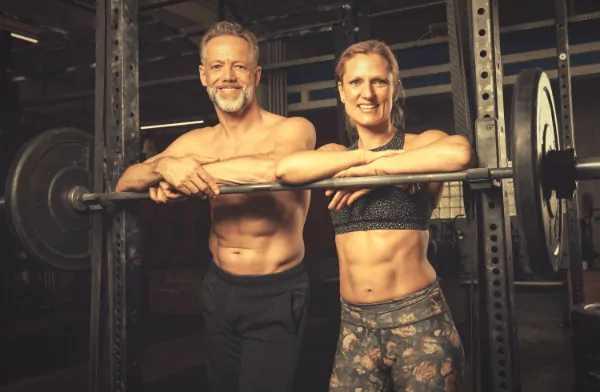 fit older couple strength training standing by squat rack leaning on a barbell